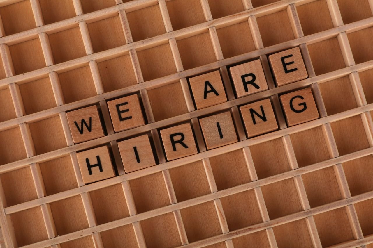 core-values Wooden letter tiles arranged to spell 'We Are Hiring' on a wooden grid background.