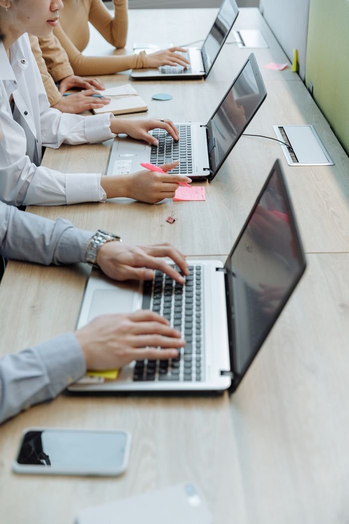 why-choose-us Group of office workers typing on laptops at a shared workspace desk.